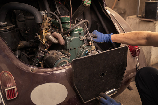 Detail of repairman checking old vehicle engine in garage