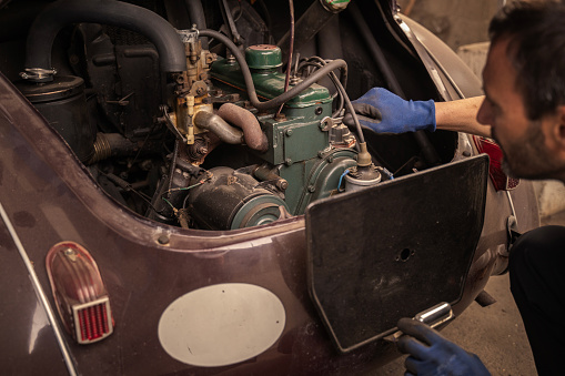 Repairman checks old vehicle motor in garage