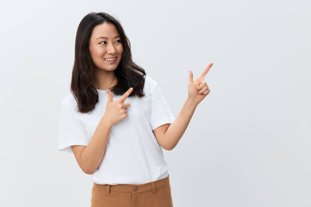 istock Lovely cheerful Korean young female in white basic t-shirt point finger aside at copy space posing isolated on over white studio background. The best offer for ad. People Lifestyle concept 2148254186