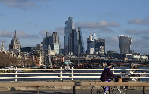 London, UK - December 17 2023:  A cyclist on Waterloo Bridge passes by the City of London skyline, the capital's financial district.