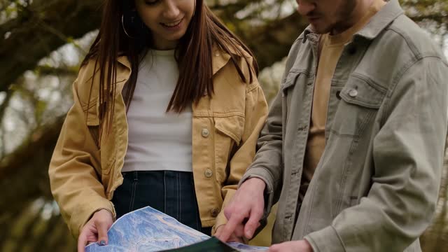 A guy and a girl with a map in hand in the forest. Navigation apps, geolocation services, tourist agencies, guides, and attractions.