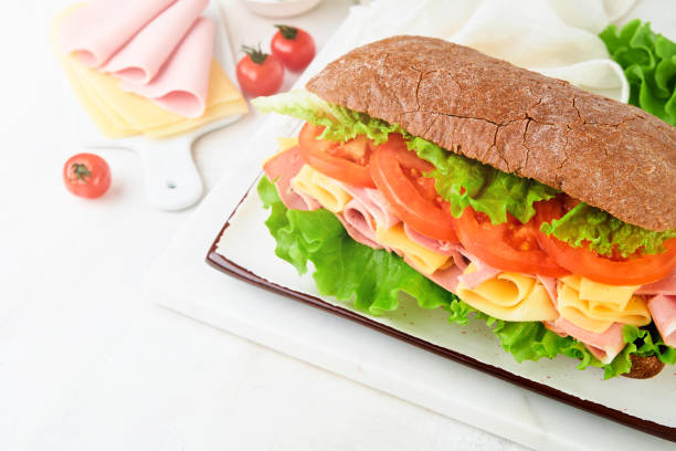 istock Sandwich. One fresh big submarine sandwich with ham, cheese, lettuce, tomatoes and microgreens on light background. Healthy breakfast theme concept, school lunch, breakfast or snack. 2148255919