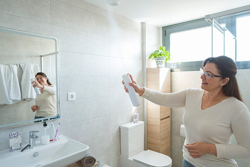 Woman spraying air freshener in her bathroom to remove unpleasant odors. High resolution 42Mp indoors digital capture taken with SONY A7rII and Zeiss Batis 40mm F2.0 CF lens