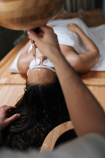 plan vertical de l’huile essentielle de shirodhara versée sur le front d’une jeune femme détendue avec des éponges en coton sur les yeux dans un salon de spa ayurvédique. - ayurveda massaging aromatherapy chakra photos et images de collection