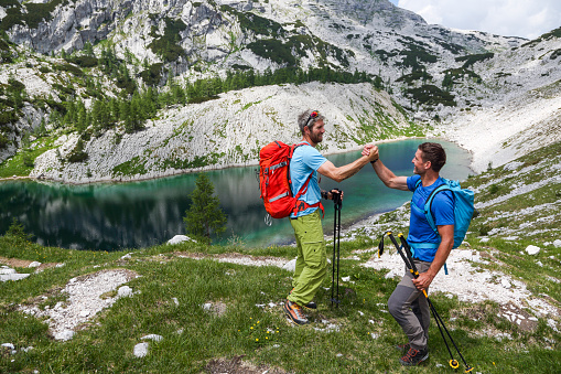 Two male friends hiking in mountains. Going to a mountain lake. Congratulating for getting here.