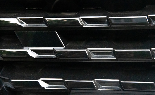 This image features a detailed view of a car's black grille with reflective chrome detailing, emphasizing the vehicle's sleek design.