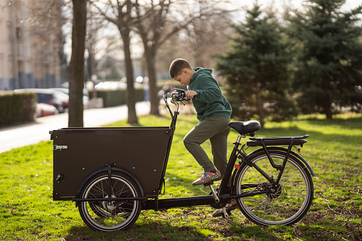 Full length shot of cute boy riding cargo bike in city park