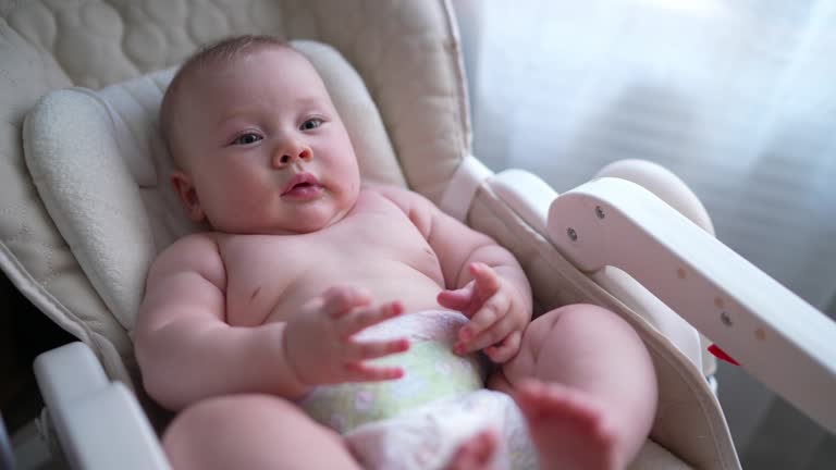 Cute newborn baby boy sitting in a white high chair next to a window. A joyful lifestyle of a happy mixed-race family. A young asian woman and active healthy baby with blue eyes in a rabbit costume. Childhood and motherhood emotions.