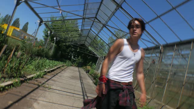 Handsome bully boy in a vibrant greenhouse setting. Man in retro style in a botanical sanctuary. A guy with a skate in a green oasis in a glasshouse.