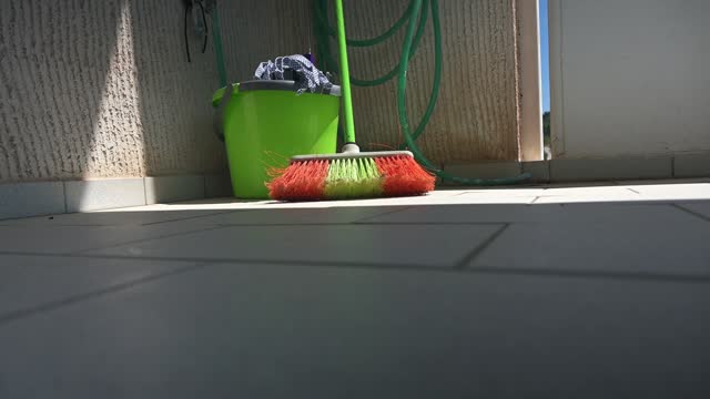 Zoom out video reveals a a broom, a bucket and a mop leaning against a wall.