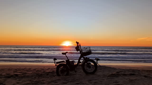 Silhouette of an electric bicycle tricycle on a sunset beach