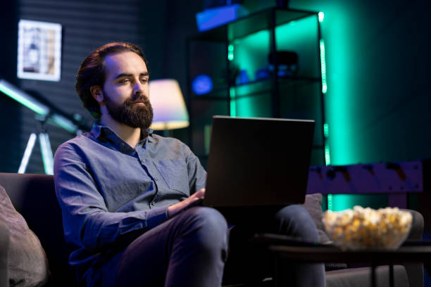 istock Man typing on laptop keyboard, watching TV with bowl of popcorn ready 2148263320