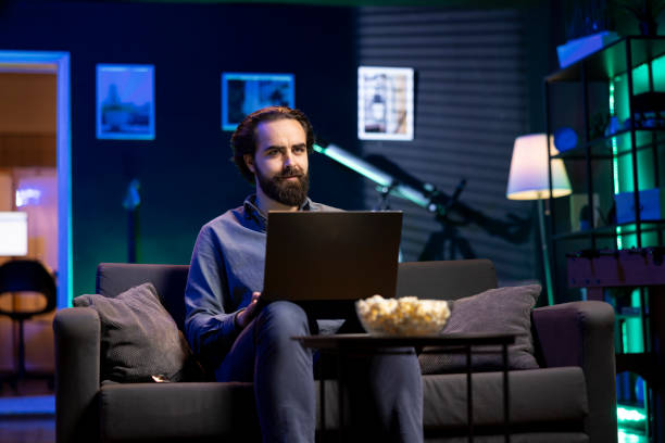 istock Man enjoying popcorn while watching TV and sending emails on laptop 2148263345