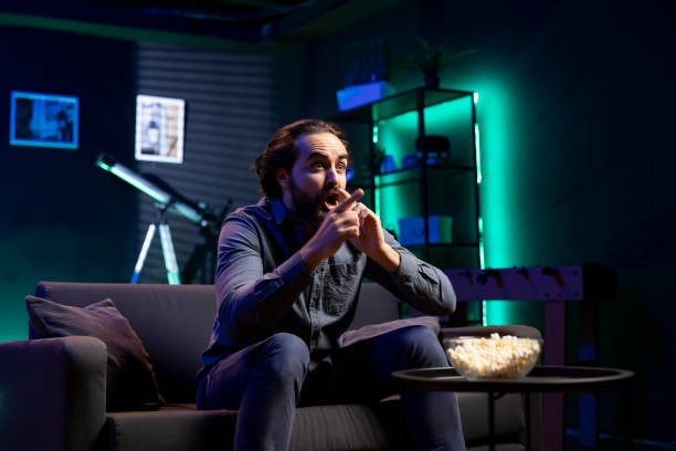 istock Man watching shows on TV, eating popcorn, reacting with surprise to plot twist 2148263504