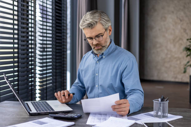istock Mature successful financier accountant working with documents papers inside the office, senior gray-haired man thinking and serious about paper work, businessman checking reports and contracts 2148264286