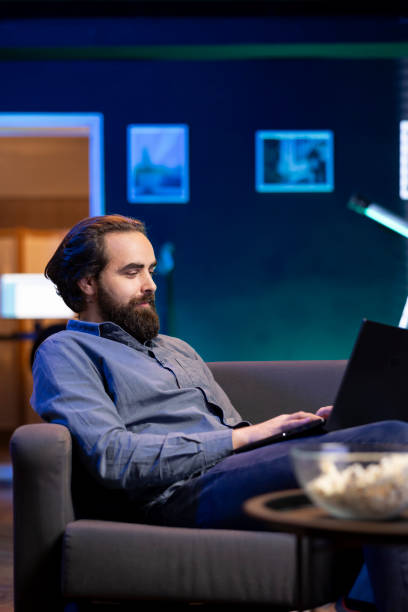 istock Man enjoying popcorn while watching TV and scrolling on social media on laptop 2148265309