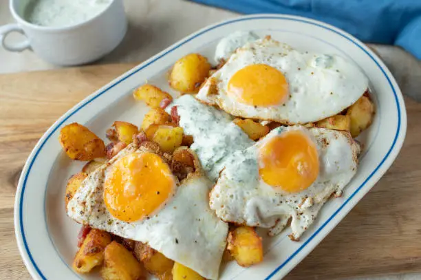 Fried potatoes with fried eggs sunny side up and herb sauce on a plate. Ready to eat