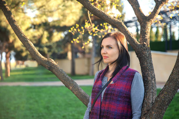 Woman leans against a tree and looks away smiling