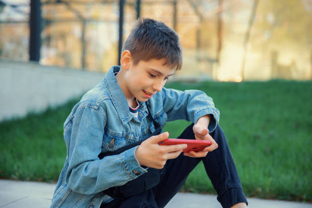 istock Boy sitting in the park and playing on the phone 2148267598