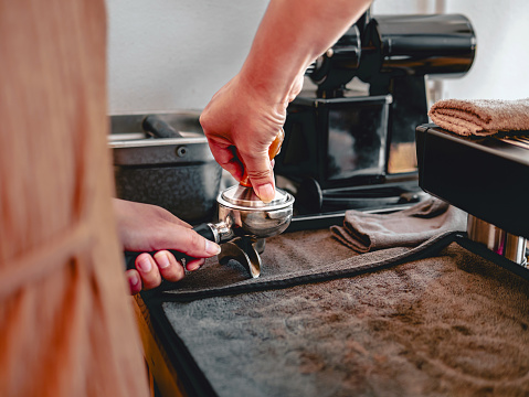 Barista presses ground coffee using a tamper in a coffee shop