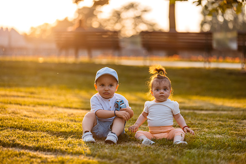 Male and female toddlers sitting on the grass in the park.