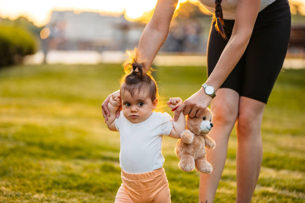Beautiful young mother teaching her daughter how to walk in the park.