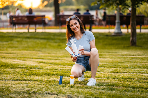 Portrait of a beautiful young woman holding up blank products in the park.
