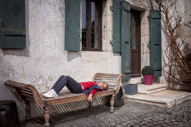 A girl enjoys a peaceful moment on an old wooden bench by a traditional house with weathered green shutters and a potted plant on doorstep.