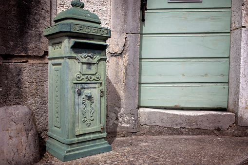 An old-fashioned green mailbox by a weathered door with shutters, reflecting the charm of traditional European village post.