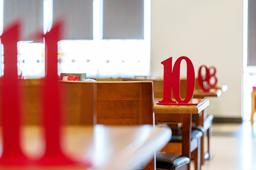 A bright red numeral 10 stands prominently on a wooden table in a restaurant, with soft sunlight filtering through the windows, casting a warm glow onto the neat, empty seating area, awaiting patrons.