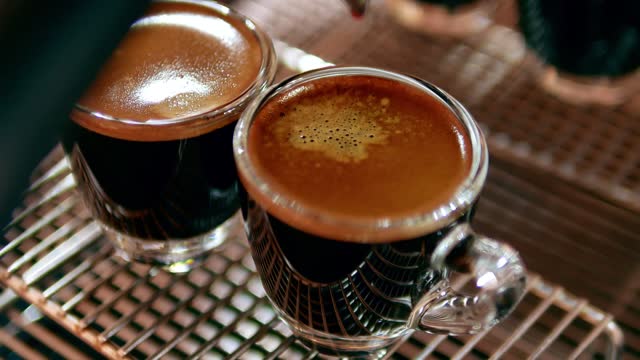 Close up of Espresso shot with coffee crema and Professional coffee machine while preparing two espressos shot glass in a coffee shop.4k video