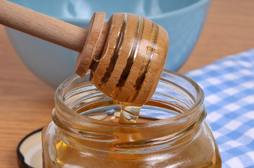 Liquid honey flowing from a wooden honey spoon into a honey pot