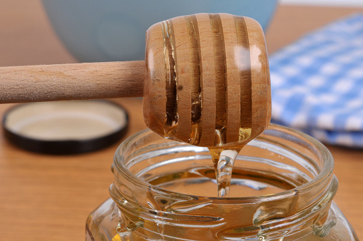 Liquid honey flowing from a wooden honey spoon into a honey pot