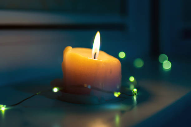 Burning candle with a small garland standing on a windowsill late in the evening night.poor christmas holiday.