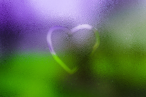 One heart drawn on dewy window glass, fogged with raindrops.Selective focus.