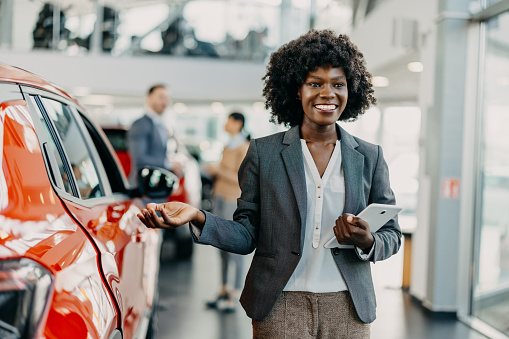 The sophistication of the showroom is personified by a young African American woman, whose presence adds a layer of refinement and expertise to the car buying experience