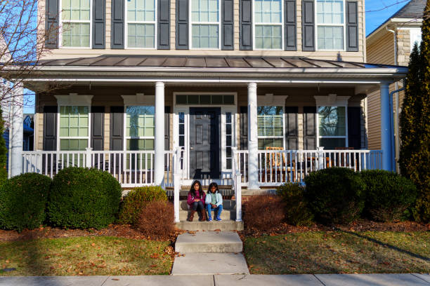 Two elementary age girls of Indian descent sit side by side on the steps to the front porch of their home and wait for the school bus to pick them up on a cool and sunny morning in Maryland.