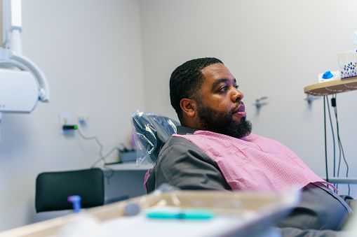 An adult man of African American descent sits patiently in a dental chair, waiting for his regular check-up to begin.