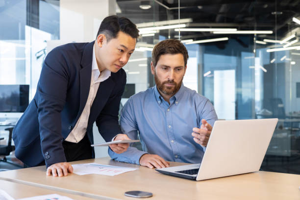 istock Two businessmen in suits work in the office, look at a laptop, discuss work issues, have a discussion 2148281981