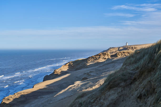 Distant view of Rubjerg Knude lighthouse on mountain with beautiful seascape under blue sky during sunny day at Jutland, Denmark
