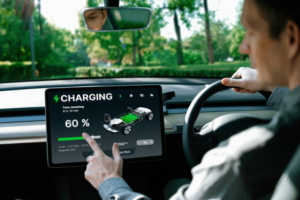 istock Electric car driver checks battery charging status app screen in car innards 2148282849