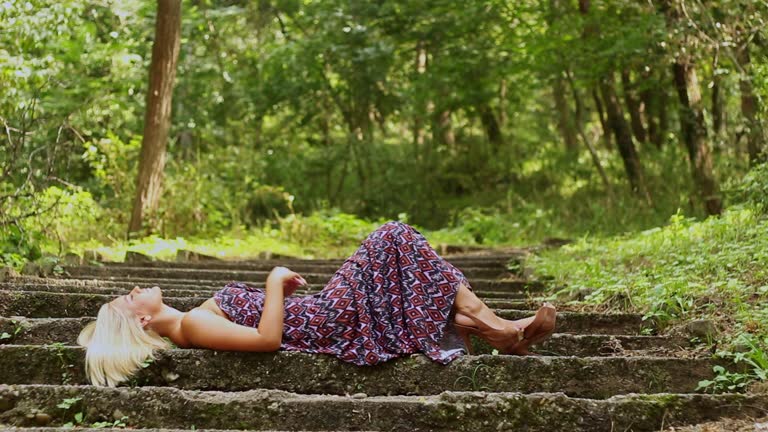 Young Woman In A Long Summer Dress Lying On Weathered Stairs In The Forest