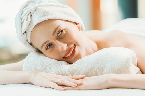 A beautiful young woman lies on a spa bed, her body relaxed and at peace. Pretty caucasian girl surrounded by the spa environment and the gentle aroma of essential oils. Close up. Tranquility.