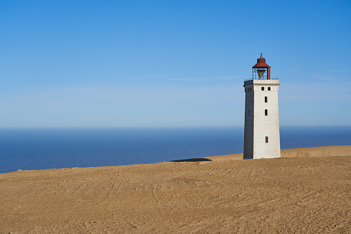 Rubjerg Knude lighthouse at coast with beautiful sea and horizon in background under clear blue sky during summer at Jutland, Denmark