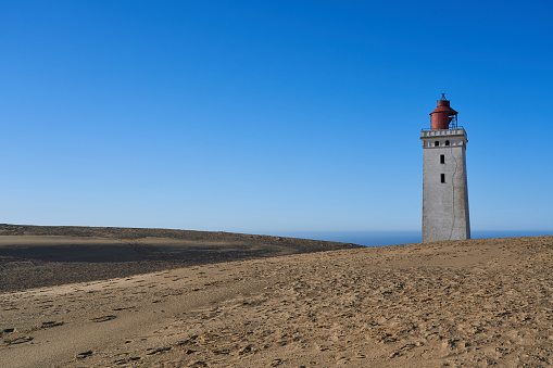View of old famous Rubjerg Knude lighthouse at sandy coast of North Sea In Jutland against clear blue sky during sunny day at Denmark