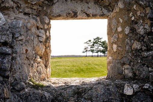 Looking through the window of a medieval castle ruin to a meadow on a sunny day in springtime.
