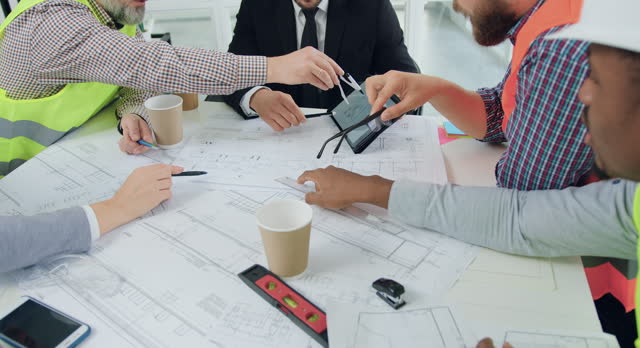 Close up of team of engineers brainstorming over construction project and comparing drawing on tablet computer during meeting