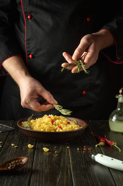 The chef adds rosemary to the pasta bowl for flavor and aroma. Work environment in hotel kitchen with spices and kitchen utensils. Copy space