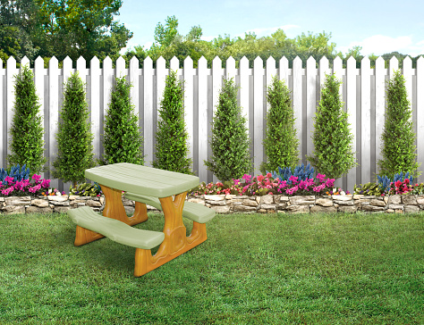 Small plastic bench in a empty backyard with green grass and white picket wood fence