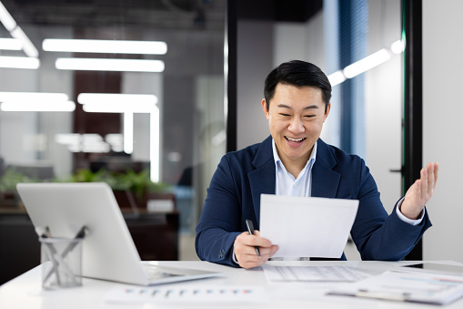 A professional businessman celebrates an achievement in the workplace while reviewing important paperwork.
